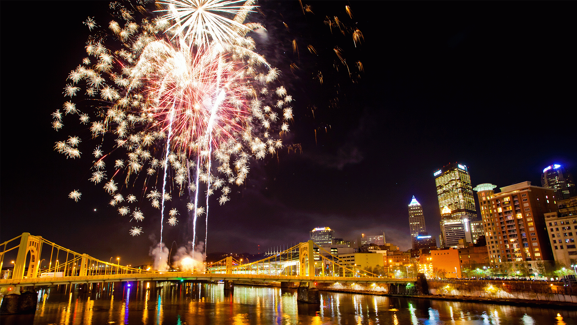 Fireworks erupt in the night sky over a bridge in Pittsburgh during Highmark Light Up Night